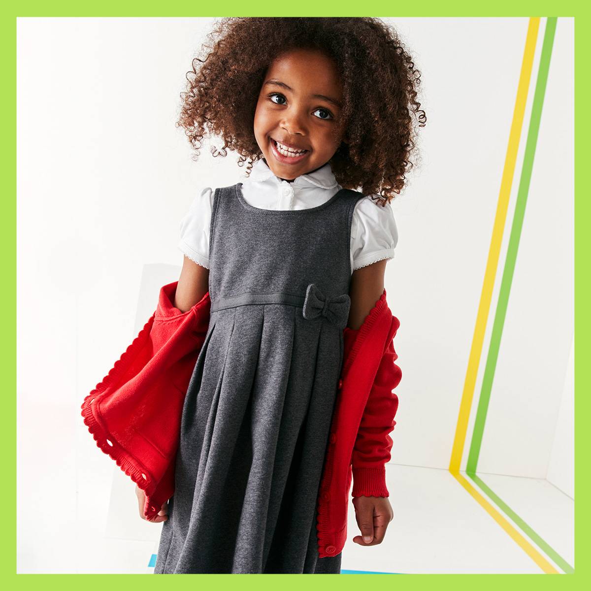 Child wearing grey pinafore and red cardigan. Shop girls’ uniform